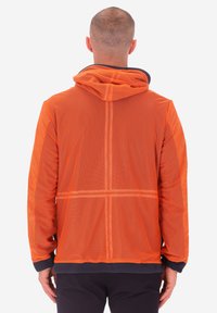 Uomo visto da dietro che indossa un giubbotto a rete arancione con cappuccio, con polsini e pantaloni scuri, su uno sfondo bianco uniforme.