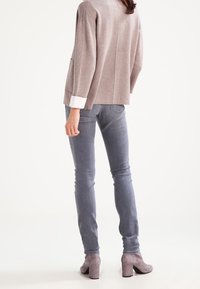 Svetle šedý svetr s volným pletením a bílým manžetou, nošený přes obepnuté tmavě šedé džíny a šedé kotníkové boty na podpatku. Jsou viditelné texturované materiály.