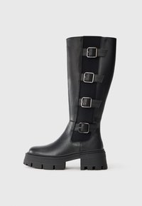 Černé kožené hol boots do výšky kolen s třemi nastavitelnými přezkami na boku, masivní gumová podrážka s drážkami pro lepší přilnavost.