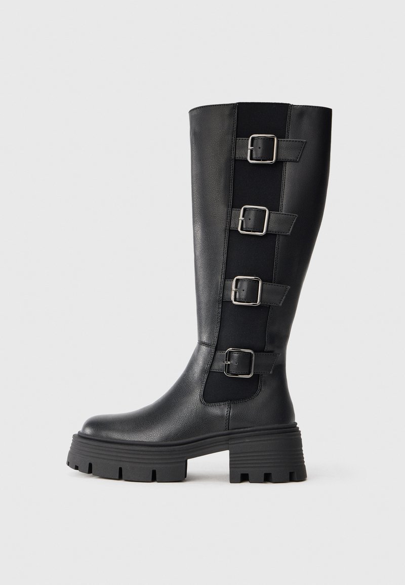 Černé kožené hol boots do výšky kolen s třemi nastavitelnými přezkami na boku, masivní gumová podrážka s drážkami pro lepší přilnavost.