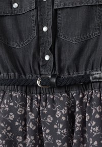 Abito in denim grigio scuro con bottoni a pressione, due tasche sul petto e una cintura intrecciata nera; motivo floreale sulla parte della gonna. Tessuto morbido.