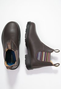 Hnědé kožené kotníkové boty s elastickými bočními panely, které mají barevný pruhovaný vzor a černé gumové podrážky.