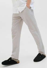Pantalons gris clair avec une coupe décontractée, texture lisse et poches latérales, associés à des sabots noirs avec une boucle décorative.