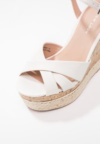 Sandalo wedge bianco con cinturini incrociati, parte superiore in finta pelle liscia, piattaforma in sughero testurizzato e interno neutro.