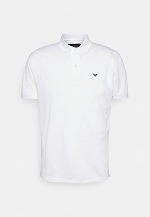 Polo blanco hecho de algodón, con una tapeta de tres botones, mangas cortas y un pequeño logo negro en el pecho izquierdo.