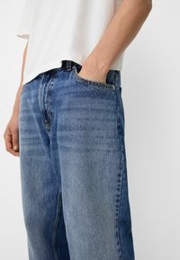 Farkut keskisinisenä, väljällä istuvuudella, haalistuneella tekstuurilla, perinteisellä viiden taskun mallilla ja hillityillä ompeluilla.