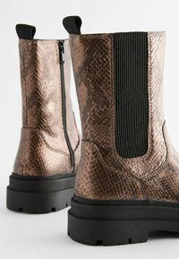 Bronzefarbene Schlangenleder-Print Ankle Boots mit einem schwarzen elastischen Einsatz, Reißverschluss und dicker schwarzer Gummisohle. Strukturmaterial mit glänzender Oberfläche.