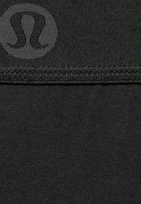 Must värviga kude, millel on pehme tekstuur ja mille vasakus ülanurgas on logo. Serval on õmblemise detail.