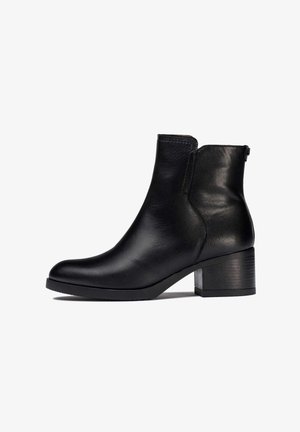 Bottine en cuir noir avec un bout arrondi, un petit talon bloc, des panneaux élastiques sur les côtés et une finition lisse.