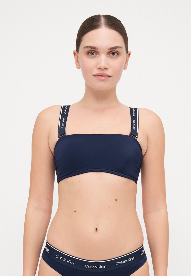 Bordo bikini top bez naramenica s širokim trakama koji sadrži bijelu oznaku "Calvin Klein". Glatki materijal s tačno prilagođenim oblikom.
