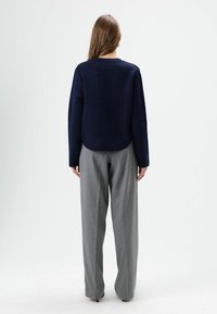Pull en maille bleu marine avec un col rond et un ourlet côtelé, associé à un pantalon large gris clair en tissu tissé.