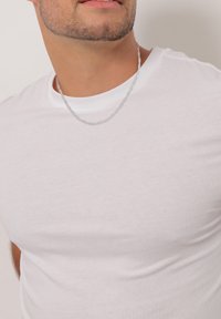 Weißes Baumwoll-T-Shirt mit Rundhalsausschnitt, taillierter Form und glatter Textur, kombiniert mit einer dünnen silbernen Kettenhalskette.