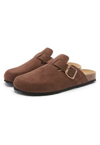Sabots en daim brun avec un bout arrondi, une sangle avec boucle en métal et une semelle en liège. La semelle extérieure présente un motif texturé pour une meilleure adhérence.