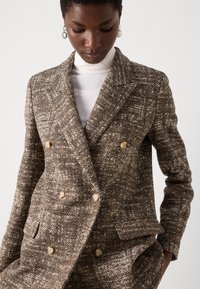 Doppelt brüstiger Fischgrätenblazer in Braun und Creme, mit großen Knöpfen und einem strukturierten Stoff sowie einem geformten Revers.