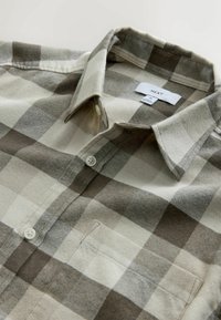 Lekką koszulę flanelową w beżowo-brązową kratę. Kołnierzyk z guzikiem, jedna kieszeń na piersi, miękka tekstura i luźny krój.
