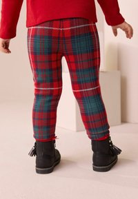 Leggings a cuadros rojos y verdes con una textura suave y cinturilla elástica, combinados con botines negros con acentos de borlas.