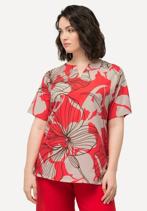 Haut floral rouge à manches courtes et décolleté en V, avec de grandes fleurs noires sur un fond beige. Tissu doux et léger.