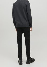 Dunkelgrauer Pullover mit Rundhalsausschnitt, kombiniert mit schwarzen Slim-Fit-Jeans und schwarzen Schuhen. Glatte Textur, schlichtes Design, minimale Details.