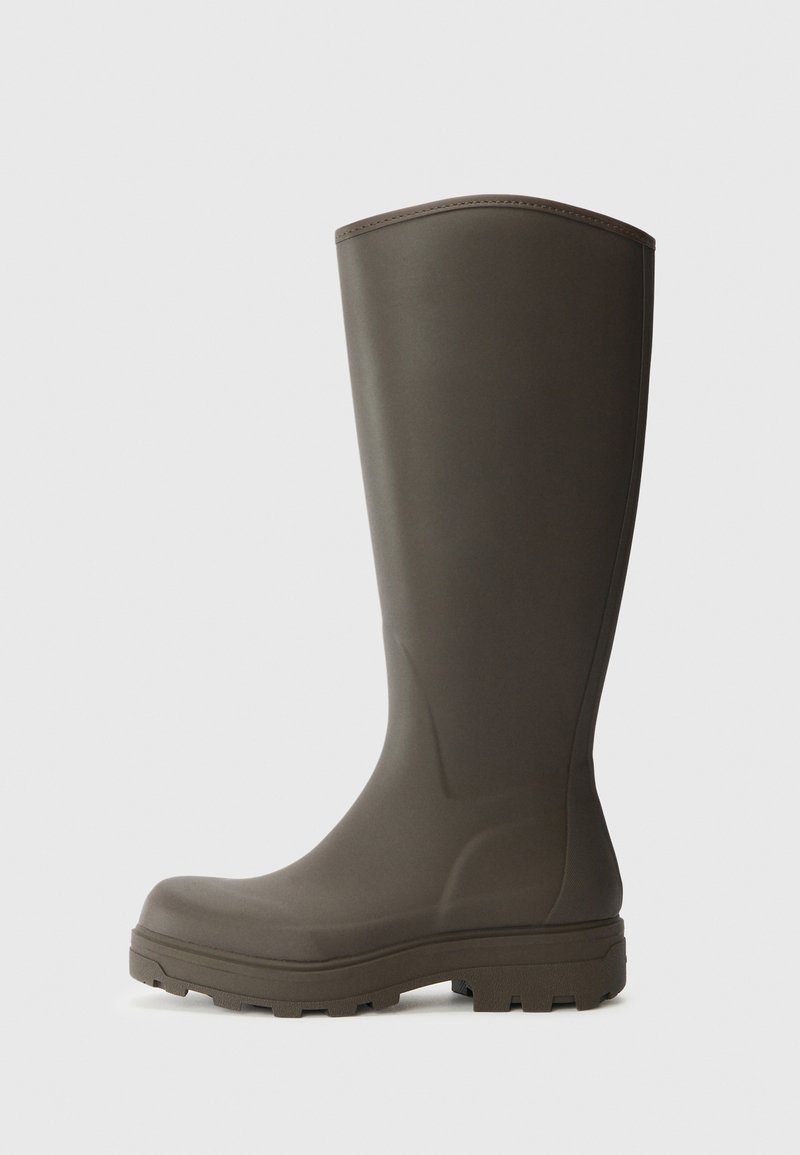 Bota de chuva de borracha castanha com sola plana, bico arredondado e acabamento liso. Altura até a metade da panturrilha com detalhes laterais sutis.