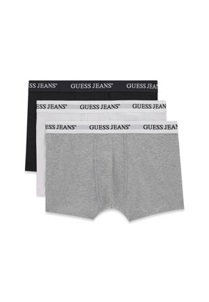 Jeune homme debout, portant un boxer gris de la marque Guess Jeans, sur fond blanc uni.