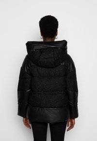 Černá péřová bunda s kapucí, vyrobená z texturované látky a lesklých akcentů. Hladký černý materiál na rukávech a lemu.