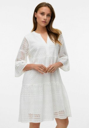 Vit spetsklänning med V-ringning och trekvarts ärmar med klockform, med intrikata mönster och lagerdesign. Lätt, texturerad tyg.