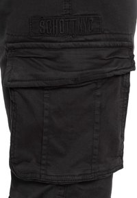 Zwarte cargobroek met een opvallende flapzak en een gestikte logopatch, gemaakt van duurzaam materiaal met een textuurrijke afwerking.