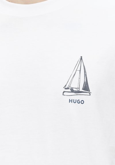 Бяла риза с малка черна графика на платноходка и думата „HUGO“ под нея в лявата област на гърдите.