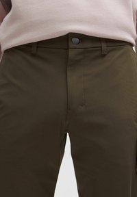 Olivově zelené kalhoty z hladké látky, s předním zapínáním na knoflíky, bočními kapsami a jemnými švy.