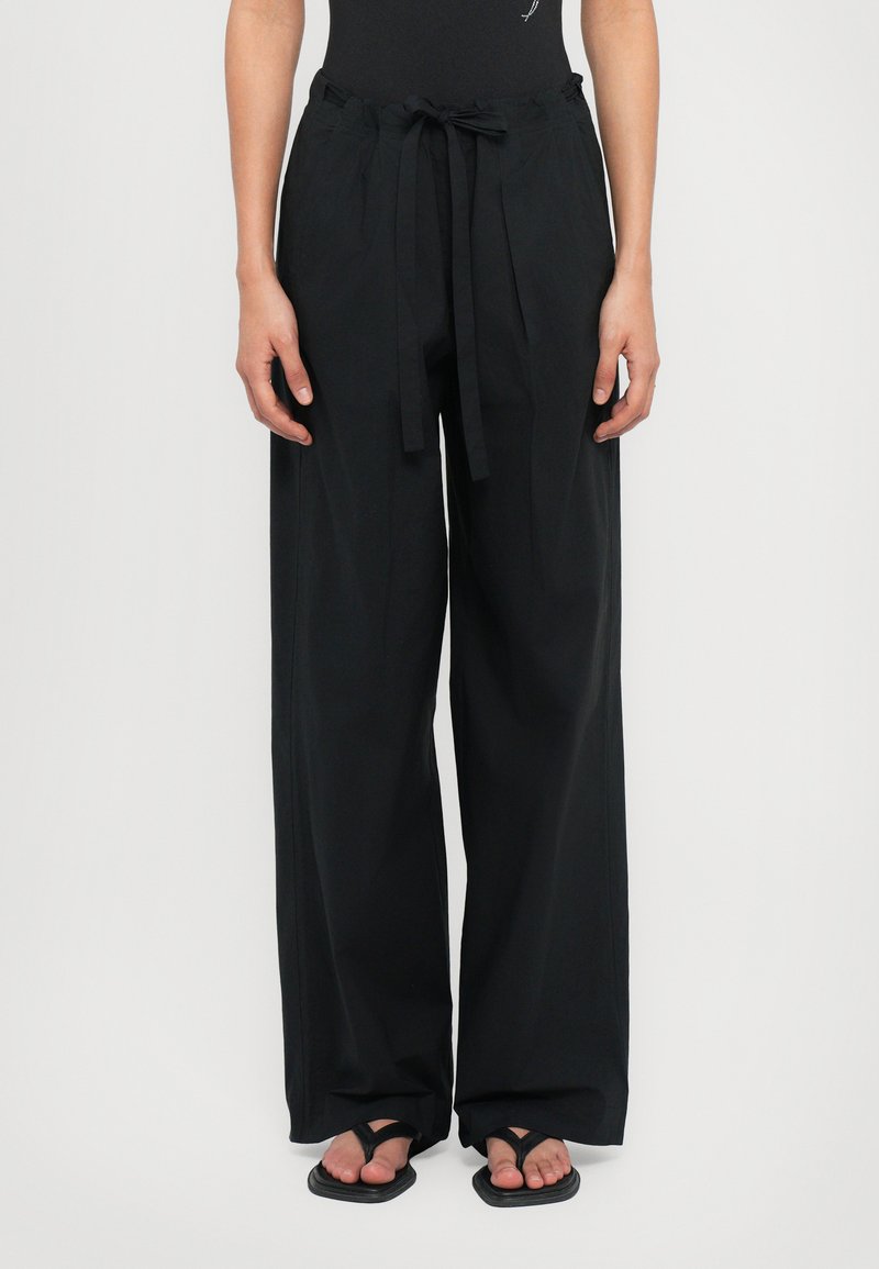 Black wide-leg pants made of lightweight fabric, featuring a drawstring waist and side pockets. Worn with black flip-flops.