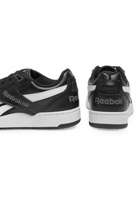Čierne kožené tenisky s bielymi akcentmi, s nízkym strihom, textúrovaným povrchom, šnurovaním a brandingom Reebok na päte.