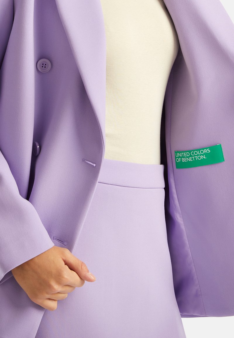 Lavendel Blazer mit zwei Knöpfen, strukturiertem Stoff und einem grünen "United Colors of Benetton"-Etikett innen. Kombiniert mit einem passenden Rock.