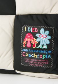 Geantă din textile matlasată, cu panouri negre și crem. Pata centrală prezintă broderii colorate cu ciuperci și o floare, acompaniate de text.