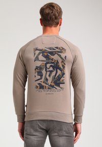 Beige sweatshirt with a textured back graphic in dark blue, green, and orange abstract patterns, featuring a curved hem and ribbed cuffs.