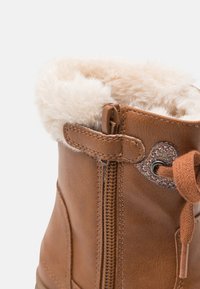 Brauner Kunstlederstiefel mit einem flauschigen, cremefarbenen Futter, Reißverschluss und einem herzförmigen Glitzerelement an der Seite.
