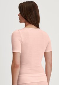 Top a maniche corte a costine in morbido tessuto rosa. Presenta un collo arrotondato e una silhouette aderente, enfatizzando una texture liscia.