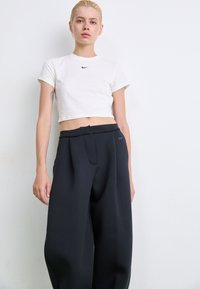T-shirt blanc court avec un logo Nike noir, associé à un pantalon large noir avec une poche avant et un détail de logo subtil.