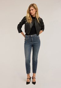 Chaqueta de cuero negra corta con textura acanalada, combinada con jeans ajustados de tiro alto azul y tacones negros de punta.
