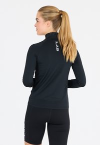 Zwart sportief langmouwtop met hoge kraag, voorzien van een reflecterende logo aan de achterkant en een getailleerd ontwerp. Gladde, rekbare stof.