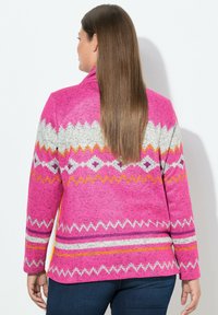 Fleecejacke in leuchtendem Pink mit Zickzackmustern in Grau, Orange und Weiß. Lange Ärmel und eine lockere Passform. Glatte Textur.