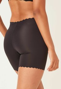 Zwarte hoge taille shorts met een gladde, rekbare textuur en gegolfde randen. De stof is mat en sluit strak aan.