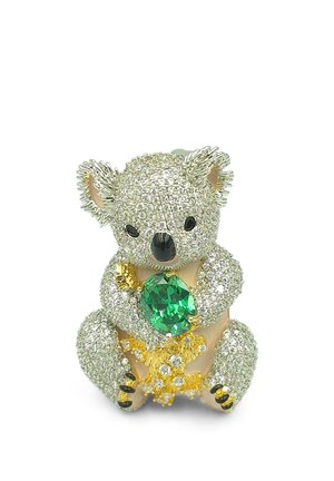 Broche en forme de koala incrustée de cristaux clairs, tenant une grande pierre précieuse verte avec des détails rehaussés d'or sur fond blanc.