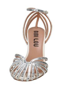 Sandal con tacco alto e cinturini argentati, con una soletta beige e una fibbia decorativa. Presenta più cinturini metallici e testurizzati disposti in un design a spirale.