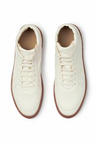 Bijele kožne tenisice s smešnim gumastim potplatom, koje imaju okrugli vrh, vezivanje na vezice i male perforacije na prednjem dijelu.