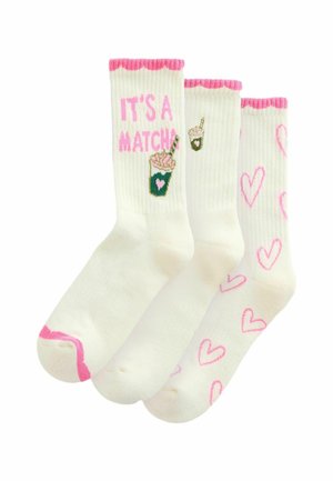 Three pairs of white socks. One with pink scalloped edges and “IT’S A MATCH” in pink, another features a drink design, and the last has pink hearts.