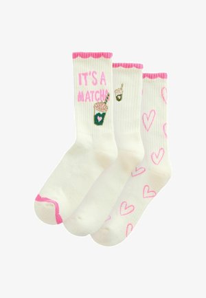 Three pairs of white socks. One with pink scalloped edges and “IT’S A MATCH” in pink, another features a drink design, and the last has pink hearts.
