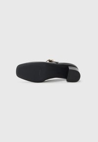 Black heeled shoe featuring a smooth leather upper, rounded toe, and a short block heel. Gold hardware detail on the side.
