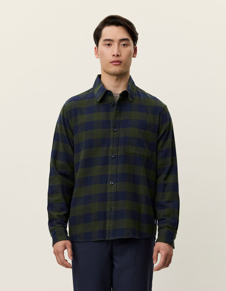 Koszula flanelowa w kraciasty wzór w ciemnozielonym i granatowym kolorze, z zapinaniem na guziki, długimi rękawami i kieszenią na piersi. Gładka faktura materiału.