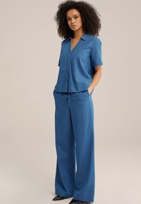 Zilā džinsa krekls īsām piedurknēm un ar apkakli, apvienots ar brīvām zilām džinsa biksēm. Apģērbu papildina melnas plakanas kurpes.