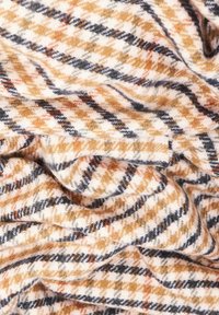 Tissu doux avec un motif à carreaux en tons beige, noir et orange, présenté en gros plan avec des plis et une texture visibles.